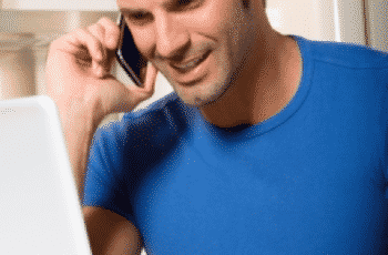 Freelancer sorrindo ao celular com camisa azul notebook e café na xícara