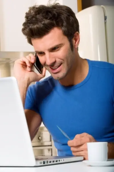 Freelancer sorrindo ao celular com camisa azul notebook e café na xícara