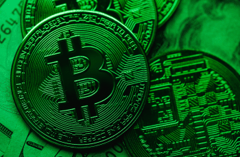 Moeda física de bitcoin iluminada em verde, indicando recuperação do mercado.