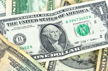 Notas de dólar americano espalhadas, simbolizando a cotação do dólar em queda no mercado.