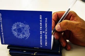 Imagem de uma mão empunhando uma caneta e escrevendo alguma coisa numa carteira de trabalho aberta